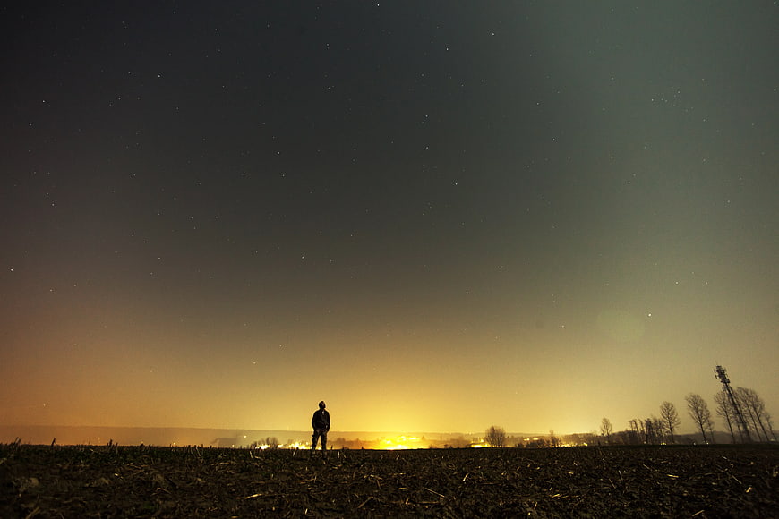 Silhouette of Man Standing in Field Under Starry Night Sky