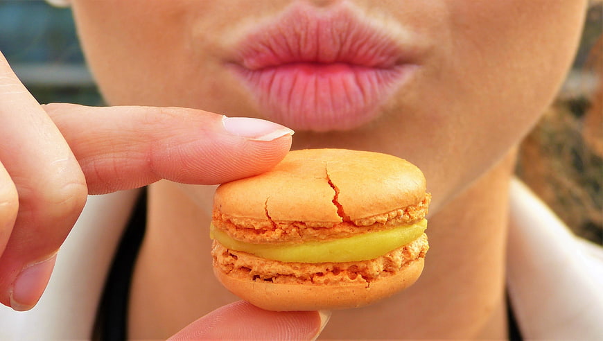 Close-up of woman holding orange macaron near lips
