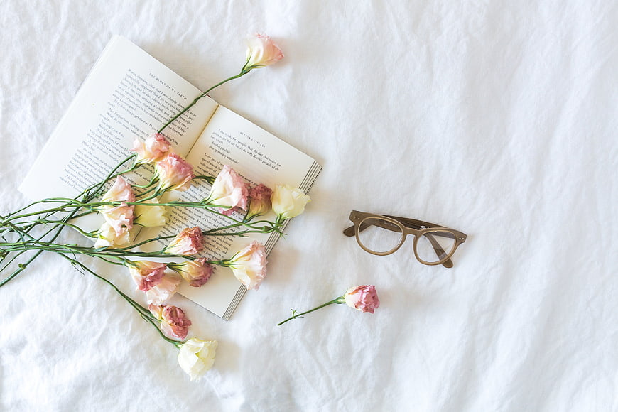 Flat lay of open book, pink flowers, and glasses on white