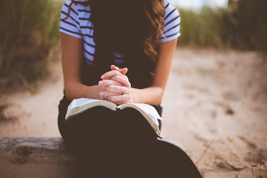 Woman Praying with Bible on Beach