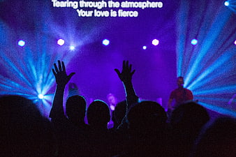 Silhouetted crowd with raised hands at a concert with purple stage lights