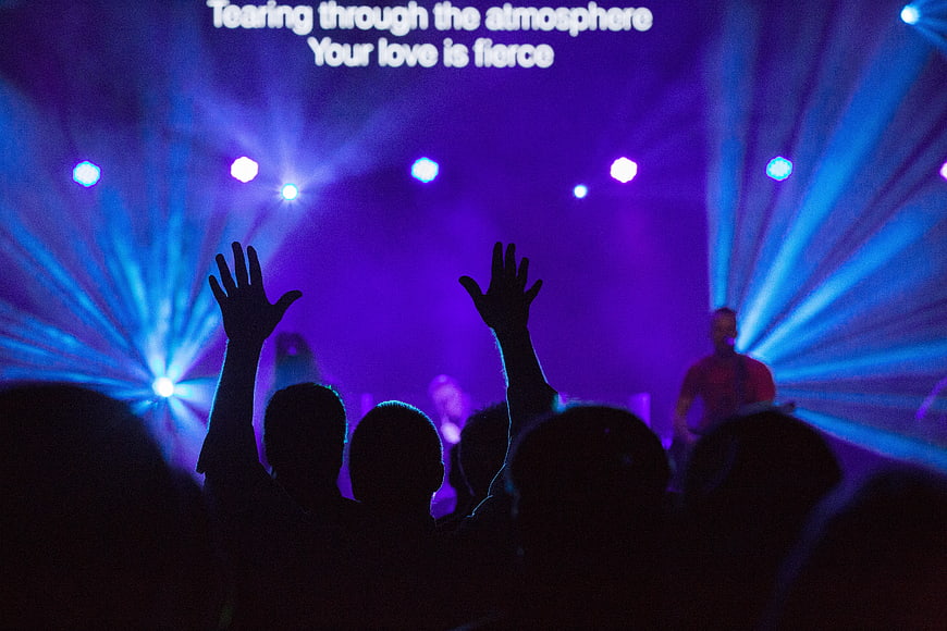 Silhouetted crowd with raised hands at a concert with purple stage lights