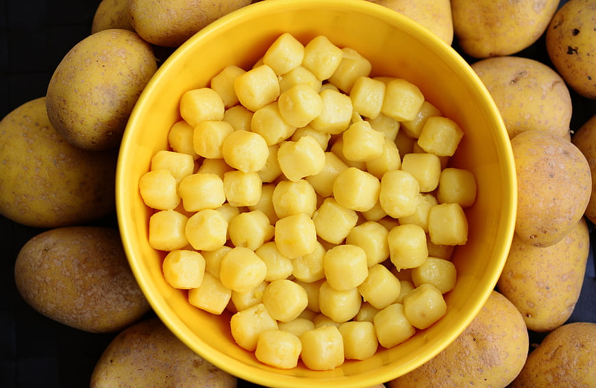 Yellow bowl of potato gnocchi surrounded by raw potatoes