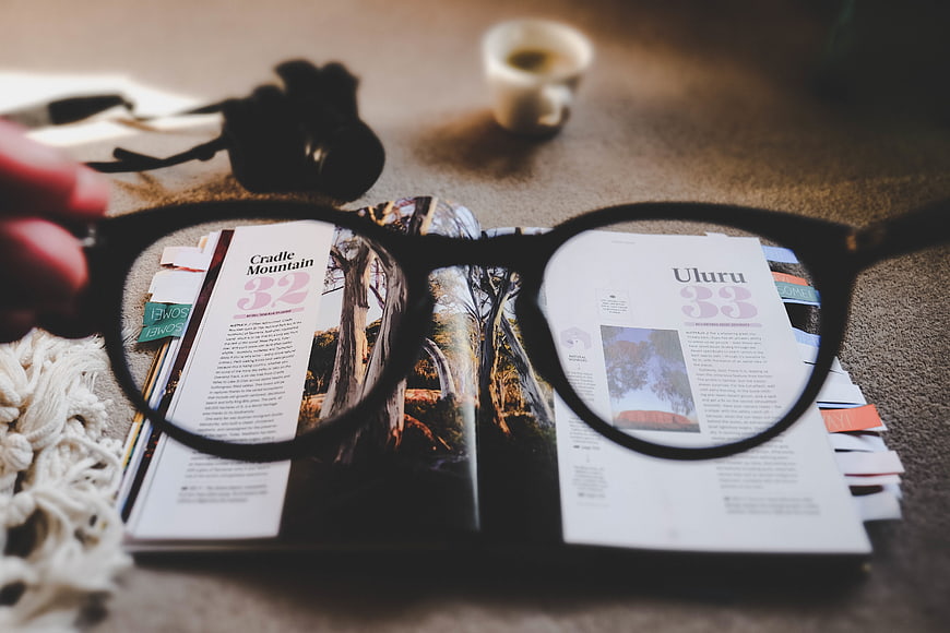 Close-up of eyeglasses held over open travel magazine