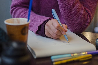 Person writing in notebook with coffee cup on table