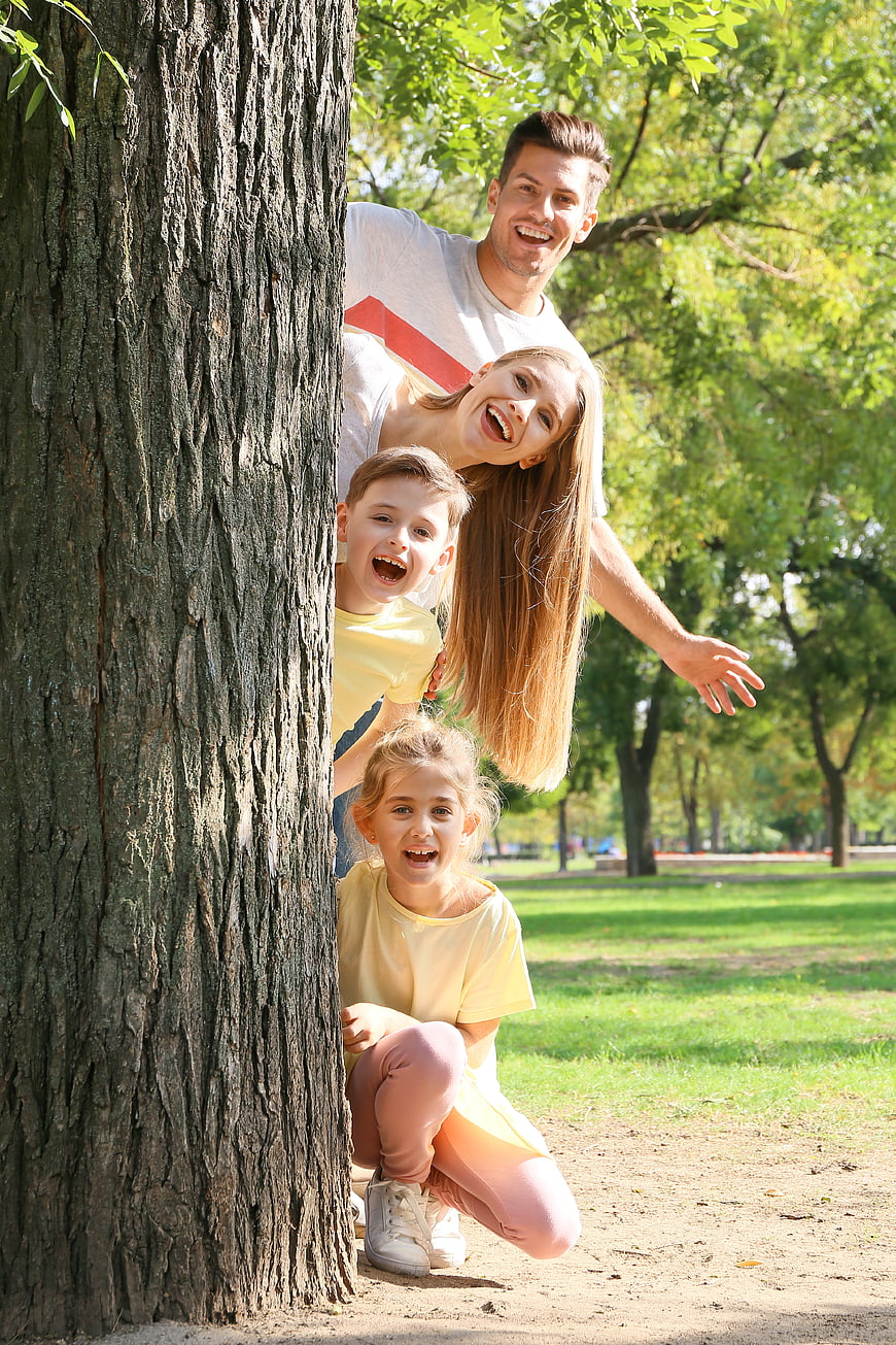 Happy family playing hide and seek behind tree in park