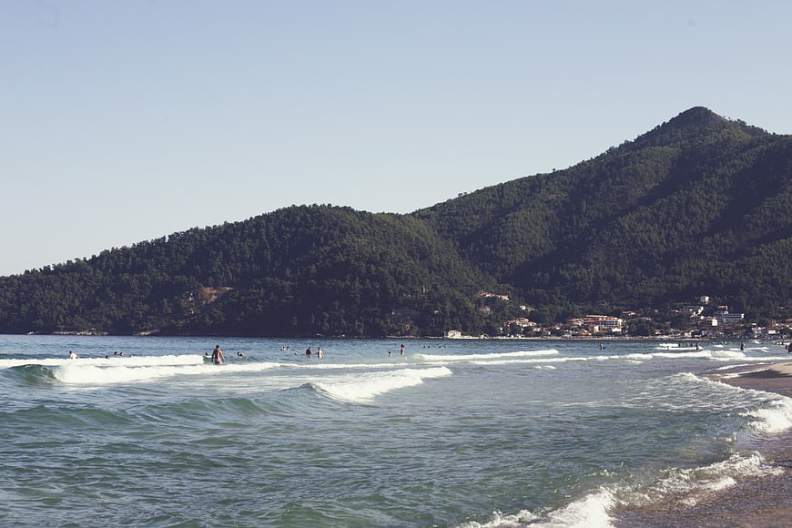 Surfers and Swimmers on a Sunny Beach with Mountain Backdrop