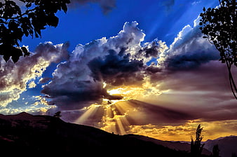 Dramatic Sunset Rays Breaking Through Clouds Over Mountain Silhouette