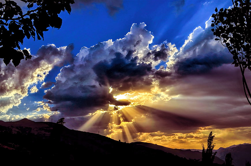 Dramatic Sunset Rays Breaking Through Clouds Over Mountain Silhouette