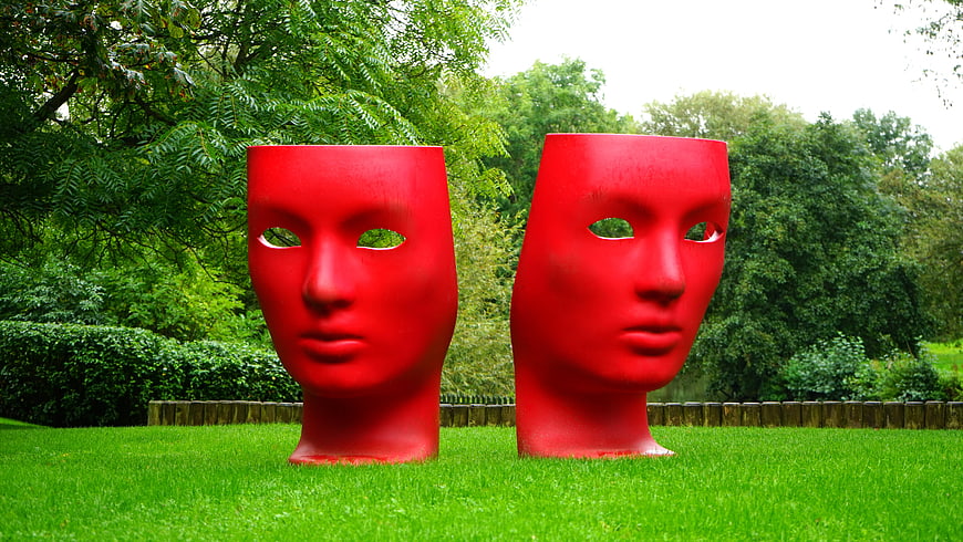 Two large red theatrical masks in a green park