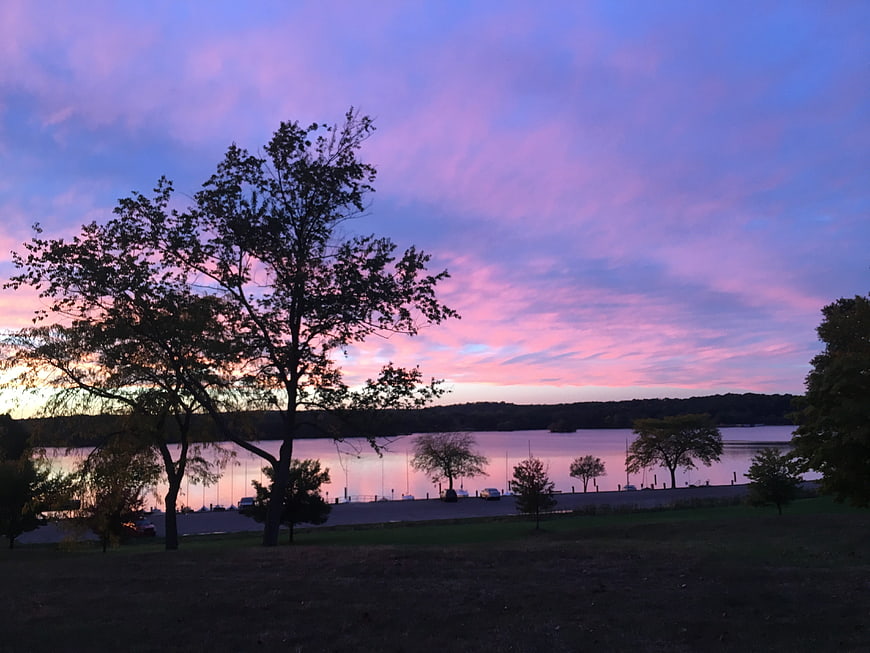 Vibrant purple and pink sunset sky over a calm lake with silhouetted trees