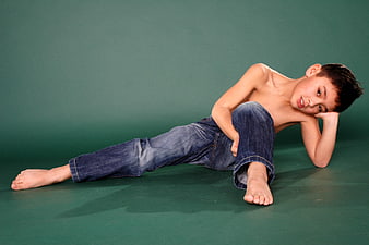 Cute shirtless boy lying on green studio background