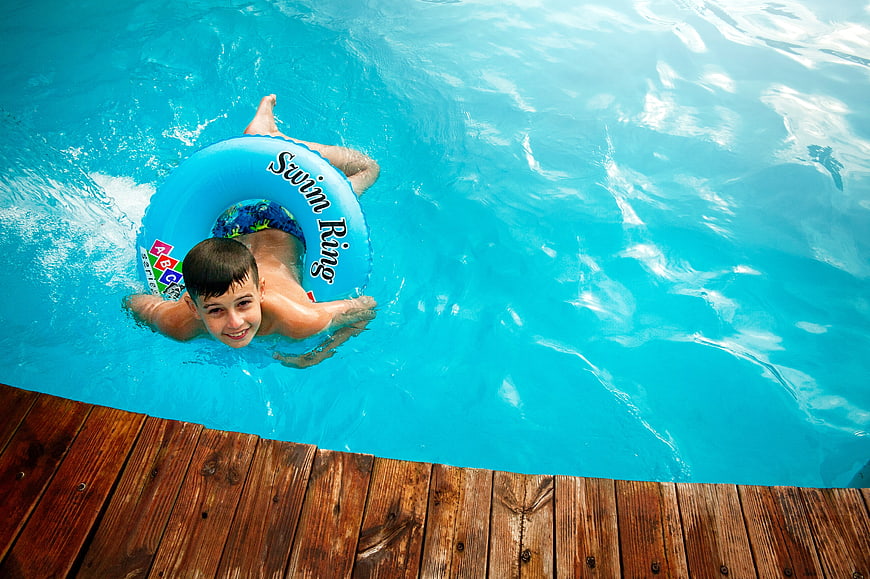 Happy Boy Floating in Pool with Blue Swim Ring