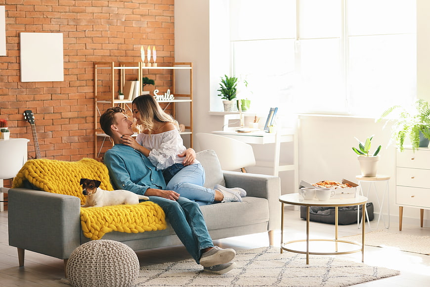 Happy couple relaxing on sofa with dog and pizza