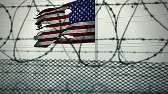 Tattered American Flag Behind Barbed Wire Fence