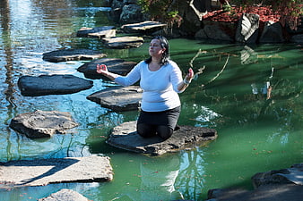 Woman meditating on stepping stones in a serene green pond