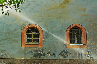 Weathered teal wall with two arched windows and sunlight beam