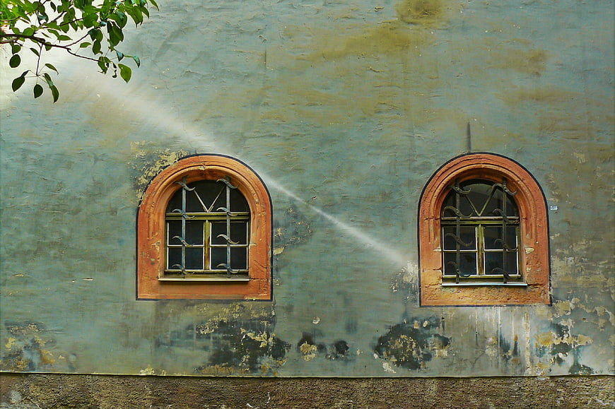 Weathered teal wall with two arched windows and sunlight beam