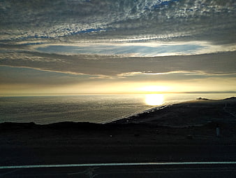 Sunset over ocean with textured clouds and dark coastline