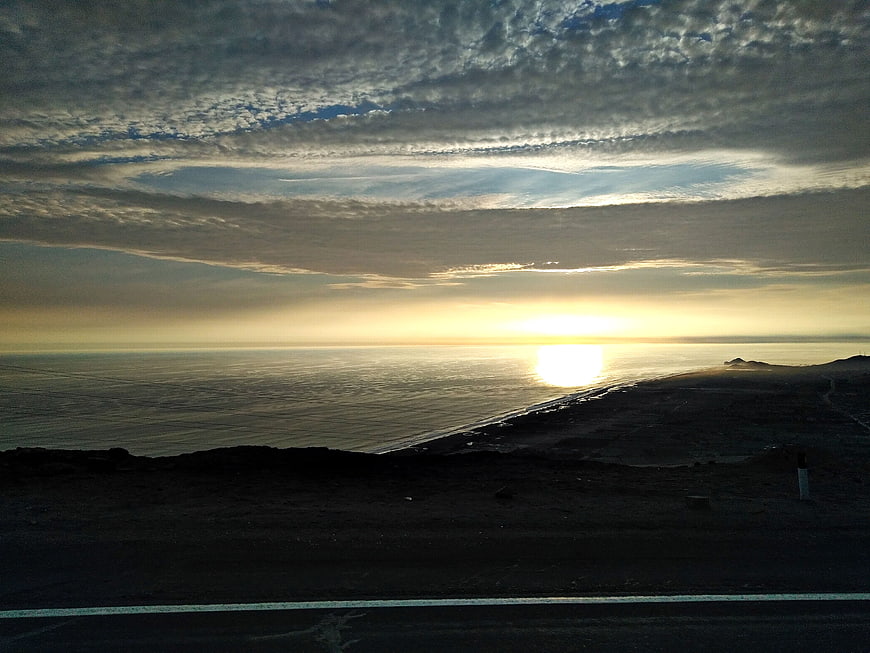 Sunset over ocean with textured clouds and dark coastline
