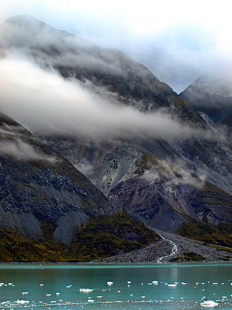 Misty mountain landscape with turquoise glacial lake and floating ice