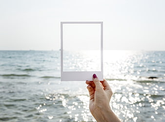 Hand holding blank polaroid frame against sparkling ocean background