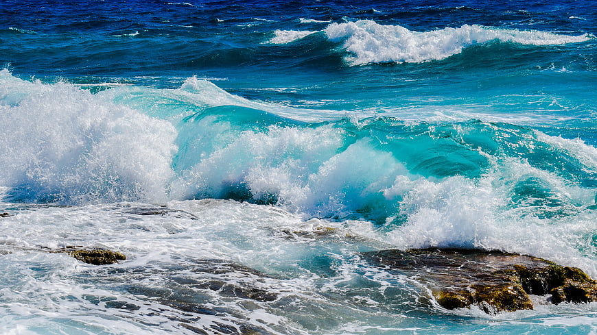 Powerful turquoise ocean waves crashing on rocky shore