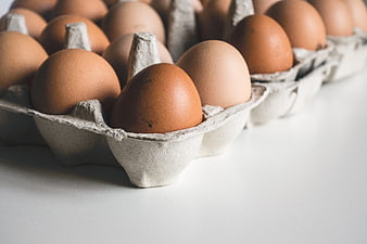 Close-up of brown eggs in a cardboard carton on white background