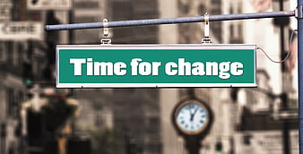 Green street sign reading Time for change with blurred clock background