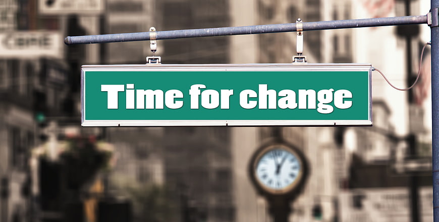 Green street sign reading Time for change with blurred clock background