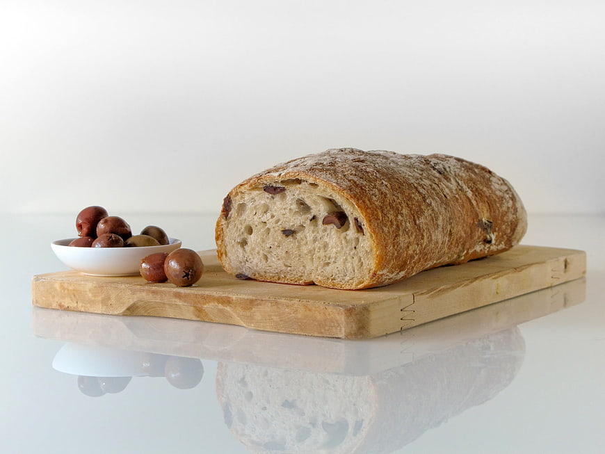 Rustic Sourdough Loaf With Olives On Wooden Cutting Board