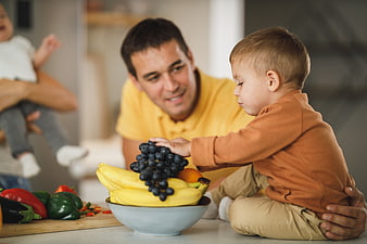 Father and toddler son eating healthy fruit in kitchen