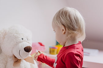 Toddler girl playing with teddy bear in bedroom