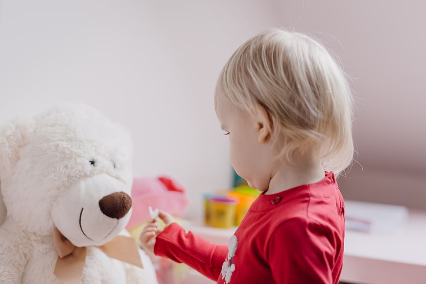 Toddler girl playing with teddy bear in bedroom