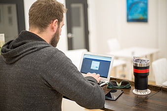 Man working on laptop at wooden desk with coffee