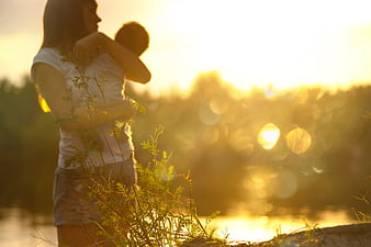 Mother holding child at sunset by the lake