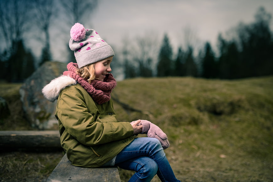 Happy young girl in winter clothes sitting on a bench in nature