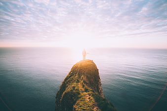 Man standing on a grassy sea cliff at sunrise