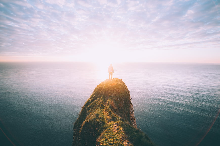 Man standing on a grassy sea cliff at sunrise
