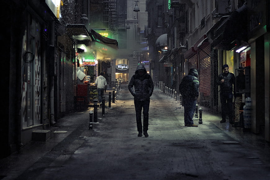Lonely Man Walking Down Snowy City Street at Night