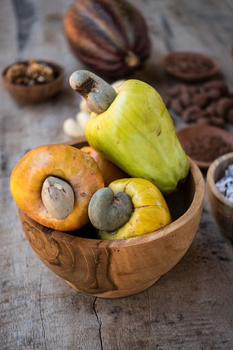 Fresh raw cashew apples and nuts in a wooden bowl