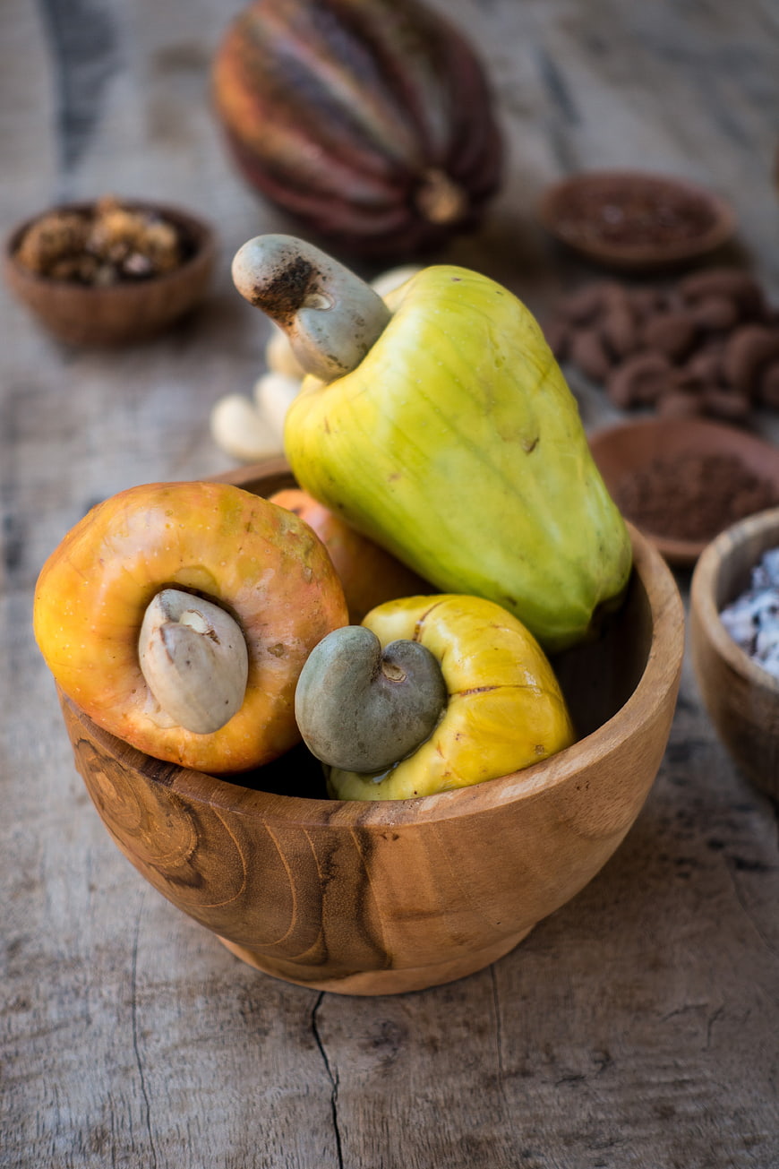 Fresh raw cashew apples and nuts in a wooden bowl
