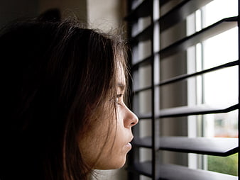 Profile of a woman looking through window blinds