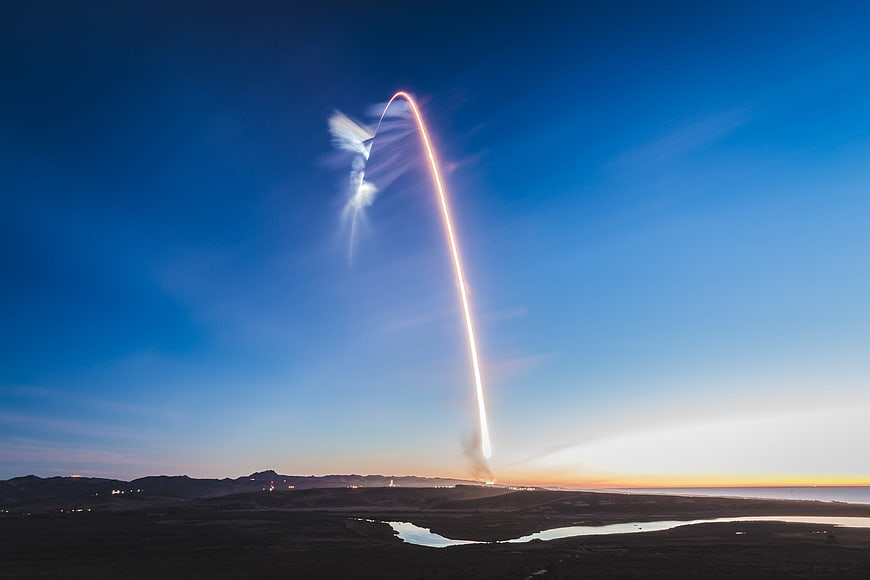 Rocket Launch Trail Arcing Over Desert Landscape at Sunset