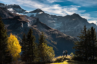 Hikers on Mountain Trail with Autumn Trees and Snowy Peaks