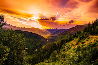 Dramatic sunset over lush green mountain valley with river