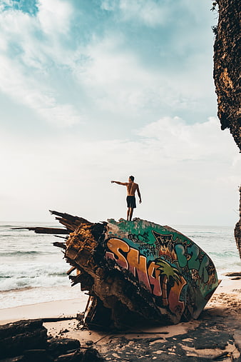 Man standing on graffiti-covered shipwreck on tropical beach