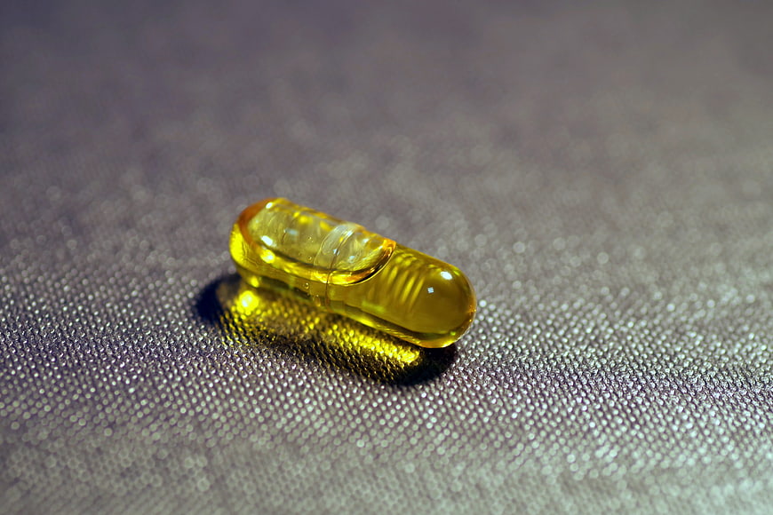 Yellow Fish Oil Capsule on Textured Gray Surface