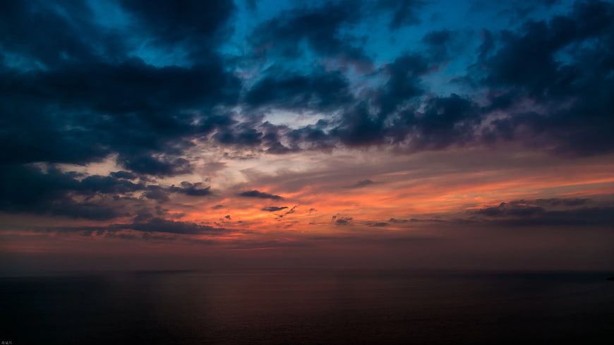 Dramatic sunset over ocean with dark clouds and vibrant orange sky