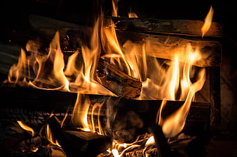 Close-up of burning logs in a dark fireplace with bright orange flames